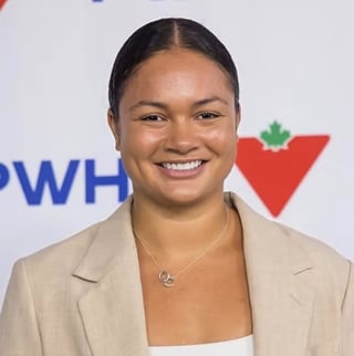 Sophie Jaques smiling, wearing a beige blazer in front of a PWHL sponsor backdrop