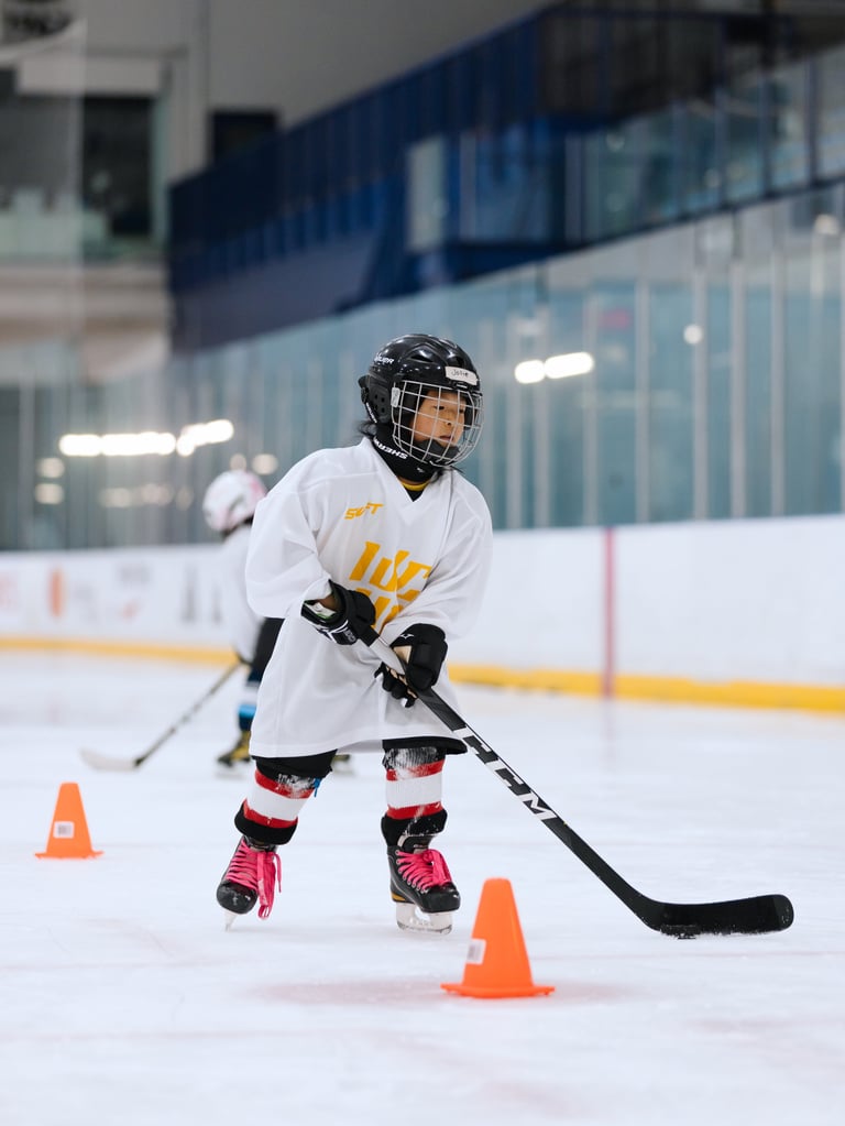 Young hockey player in white jersey number 18 skating on ice rink during training with traffic cones
