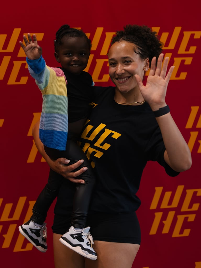 Woman holding child waving at camera in front of red and gold branded backdrop