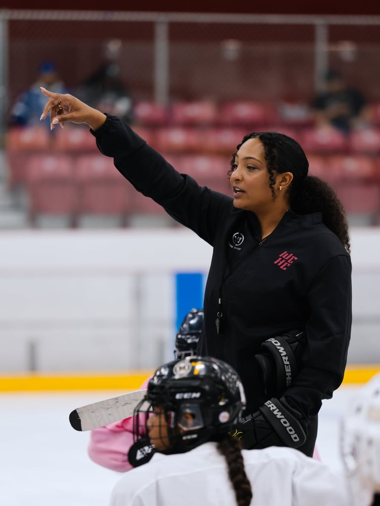 Female hockey coach instructing players on ice, pointing direction during practice at indoor arena