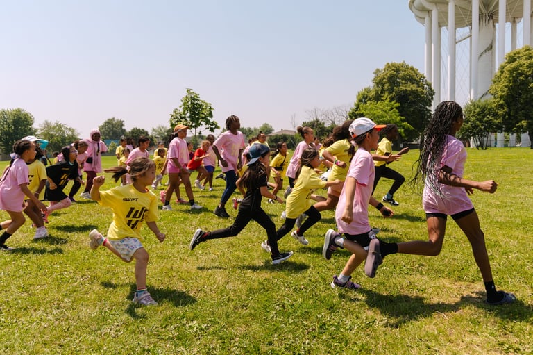 Children in pink and yellow jerseys playing together on a grass field outdoors on a sunny day