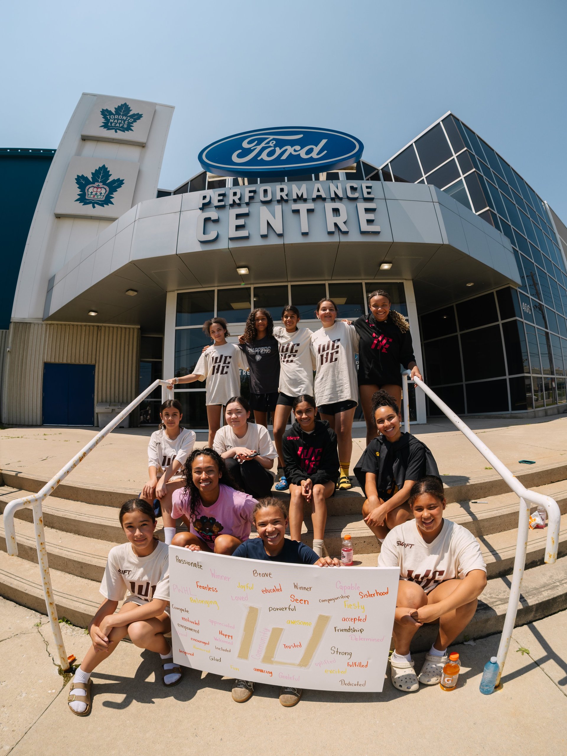 Group of people posing outside Ford Performance Centre holding a banner, with Toronto maple leaf logos visible on the building
