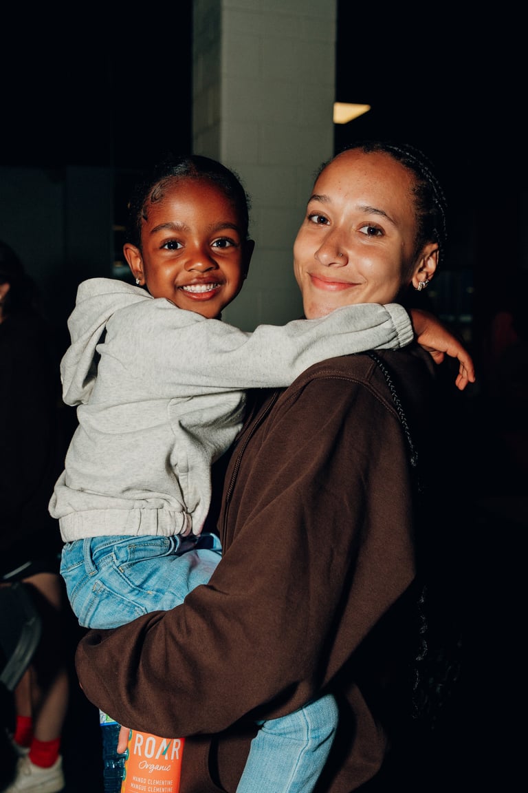 Adult woman holding a smiling young child, both posing together indoors at night