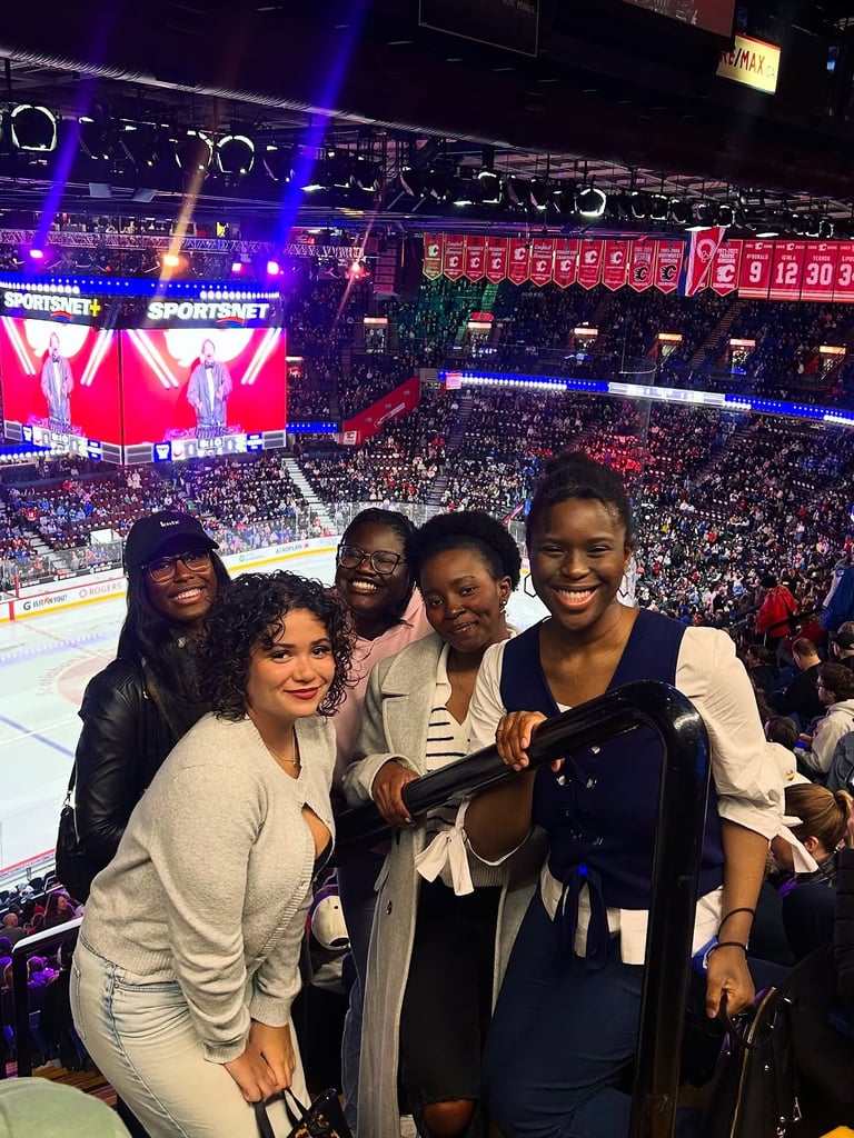Five people smiling at a crowded indoor sports arena with a large screen and scoreboard visible in the background