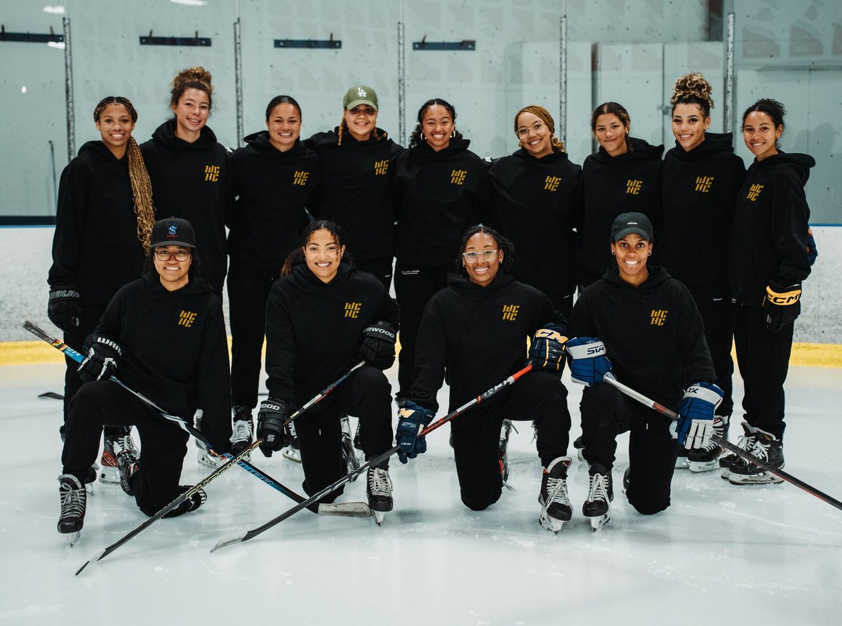 Female ice hockey team in black uniforms with gold lettering posing on ice rink