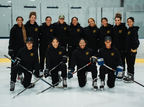 Female ice hockey team in black uniforms with gold lettering posing on ice rink
