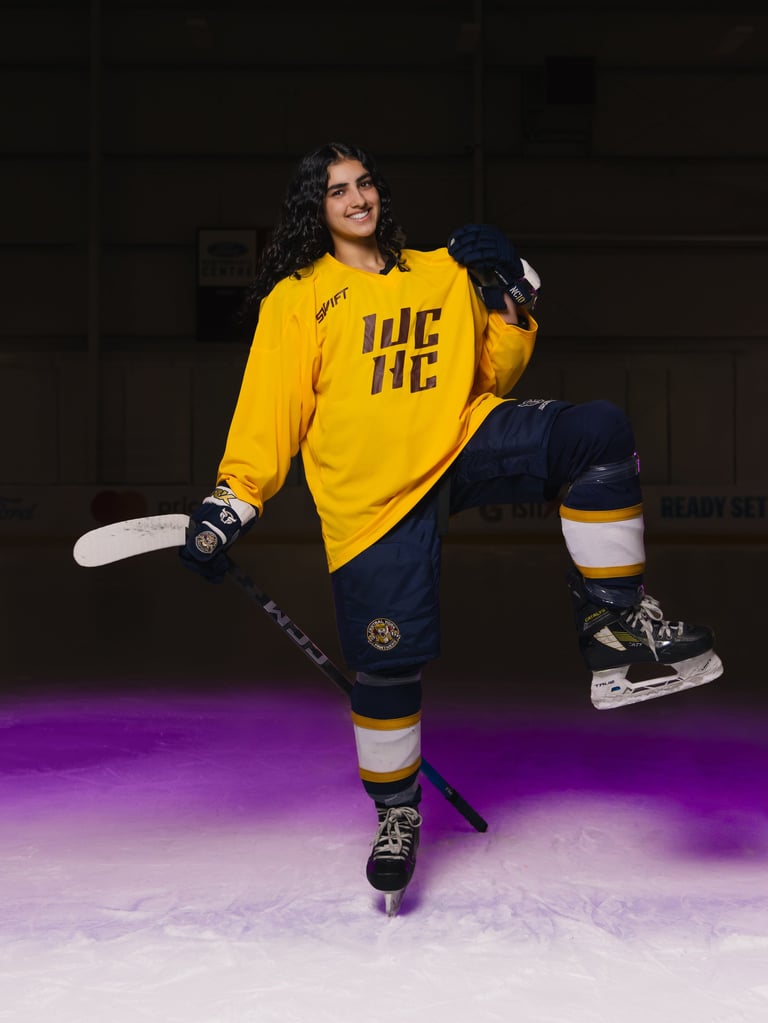 Ice hockey player in yellow and navy uniform posing on ice rink with stick and gloves