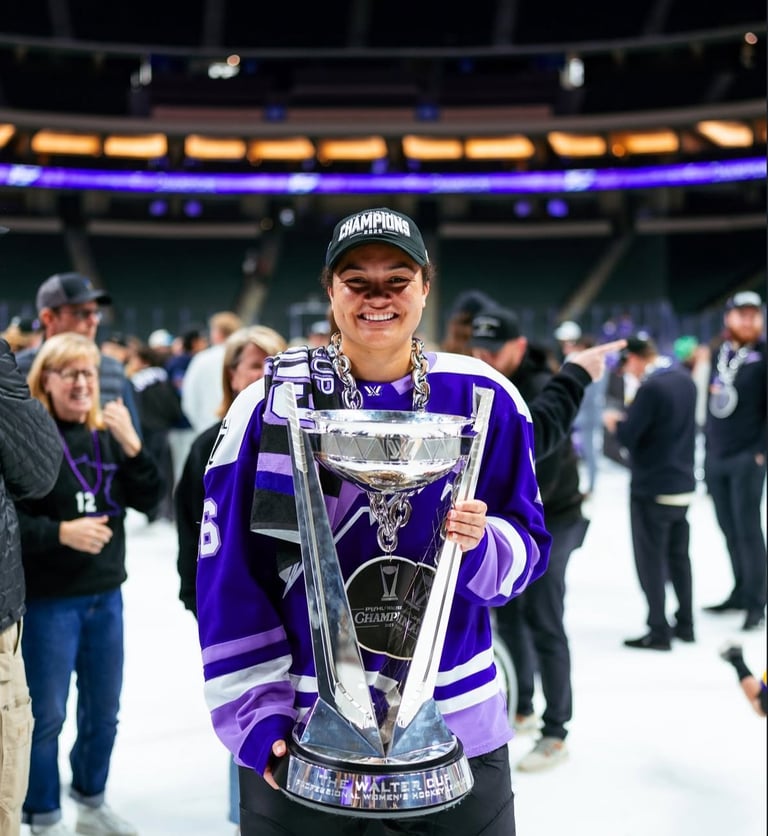 Person in purple hockey jersey holding championship trophy on ice rink with crowd in background