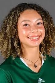 Smiling woman with curly brown hair wearing a green v-neck shirt and pendant necklace