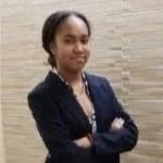 Nayla Brooks standing with crossed arms, wearing a dark blazer in front of a beige stone wall