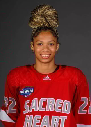 Portrait of a young woman wearing a red Adidas Sacred Heart jersey, smiling at the camera against a gray background