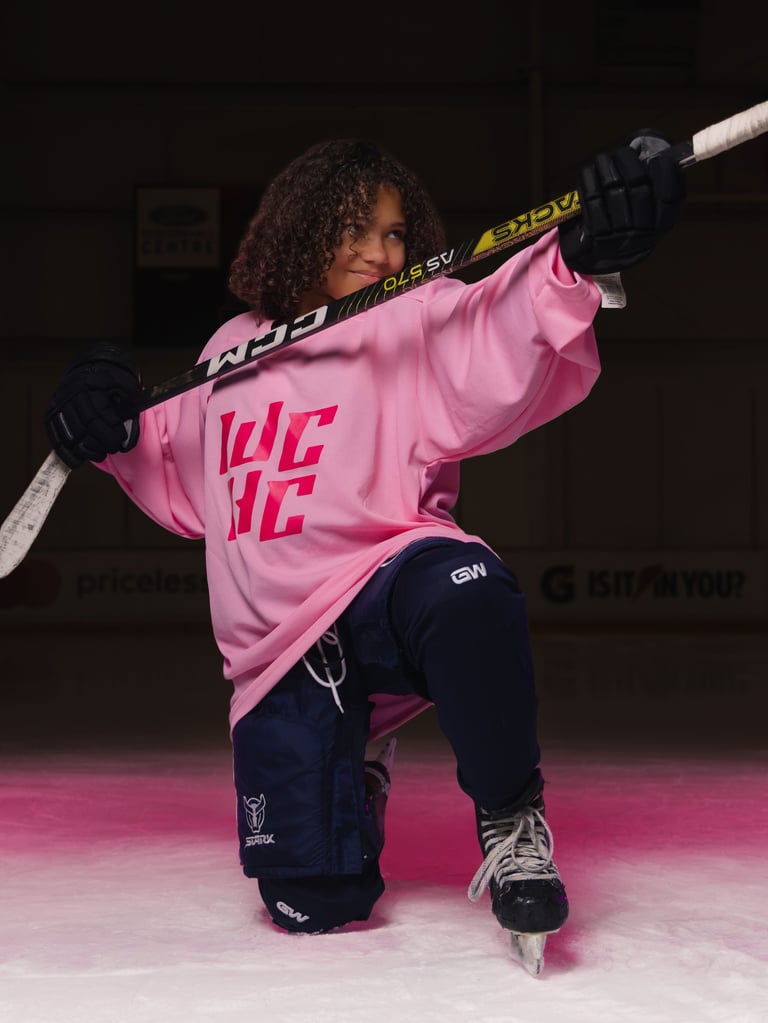 Young hockey player in pink jersey posing with hockey stick on ice rink