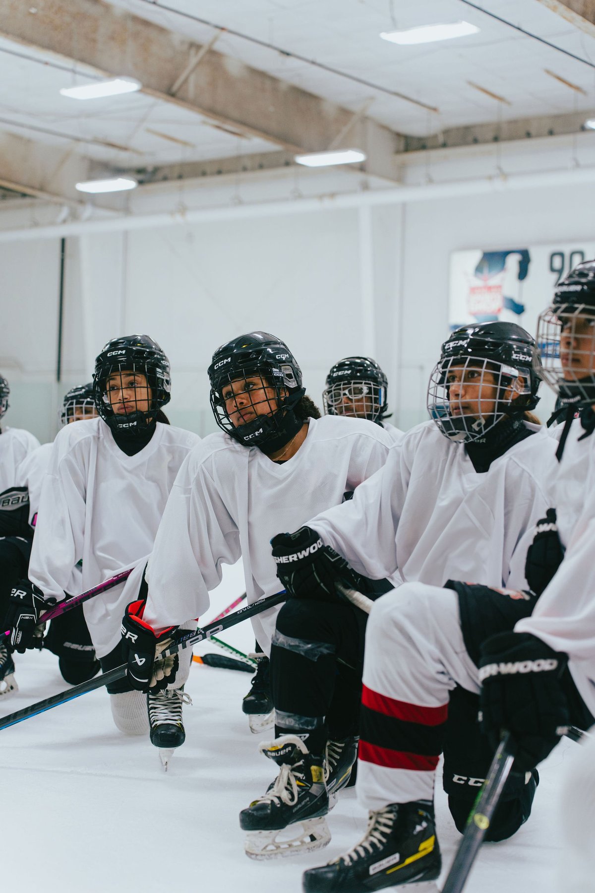Young hockey players in white and black jerseys with helmets sitting on bench in indoor ice rink