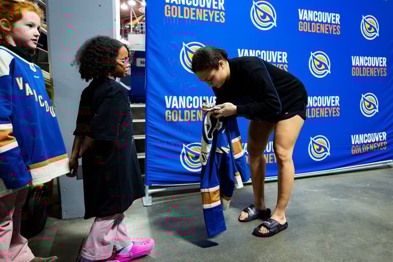 A player signs a hockey stick for a young fan at a Vancouver Canucks media event with branded backdrop