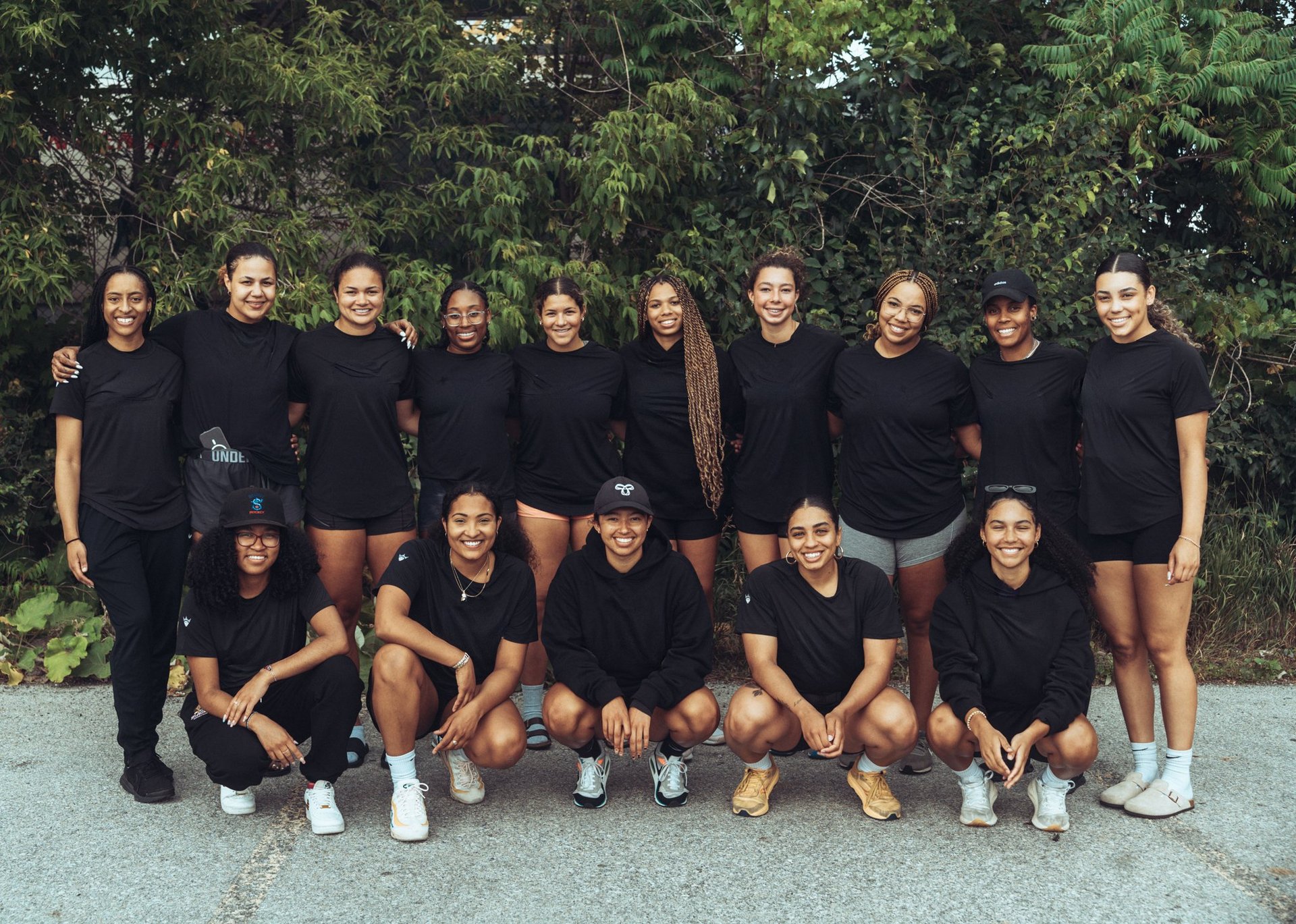 Group of people wearing black shirts posing together outdoors in front of trees