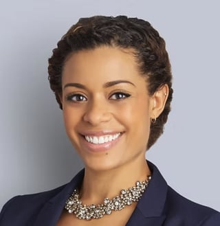 Natasha Smith with dark curly hair, wearing a navy blazer and sparkly necklace, smiling at the camera