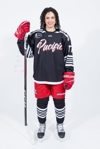 Female ice hockey player in Pacific team uniform with red and black jersey, holding hockey stick and wearing red gloves