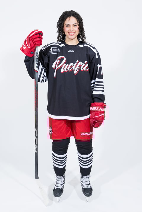 Female ice hockey player in Pacific team uniform with red and black jersey, holding hockey stick and wearing red gloves